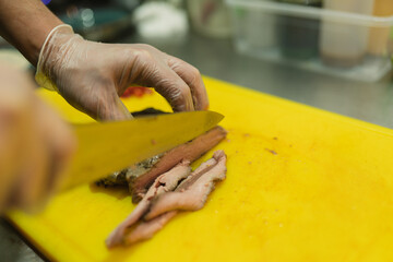 Chef in gloves uses sharp knife for slicing meat on cutting board. Professional culinarian creates...
