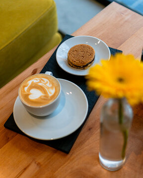 Latte and a cookie inside a city coffee shop and over a table with a yellow flower and beautiful interior design