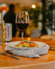 Prawns and salad launch with a cup of red wine over a wooden table on a luxury restaurant