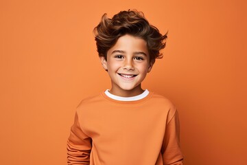 Obraz na płótnie Canvas smiling little boy in orange sweater looking at camera on orange background