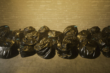 Piled High: Countless Black Garbage Bags Against a Rugged Brick Wall