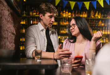 Lady helps guy in wrinkled shirt find mobile phone near bar table. Night life of young people after party in patriotic club