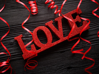love word with red ribbon over black wooden background