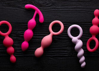 anal plugs and dildo in different shades of pink over black wooden background