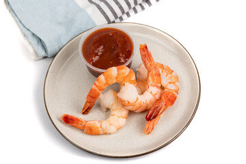 top down view of a plate of cooked, peeled jumbo shrimp on a plate with seafood cocktail sauce isolated on white
