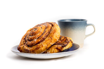 Large iced cinnamon buns, or Danish butter horns, on a plate with a coffee mug isolated on white