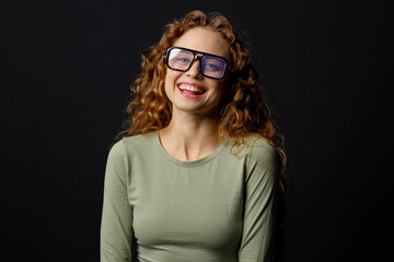 Happy smiling curly young woman wearing glasses looking at camera with joyful smile at black background - 767207591