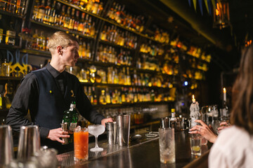 Barman takes order for cocktails from guests near bar counter. Bartender holds bottle of elite...