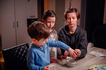 A young boy and girl, assisted by a woman, are deeply engaged in a hands-on chemistry experiment at...