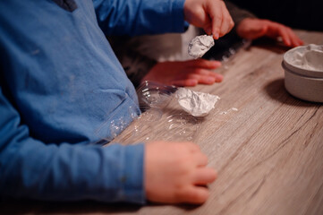 A close-up of a child's hands and the materials involved in a home science experiment, depicting the tactile experience and educational play