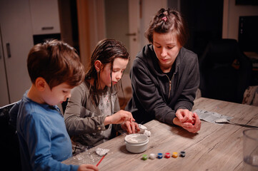An absorbed group of siblings conduct a science experiment at home under the watchful eye of a young woman, fostering a collaborative and educational family moment