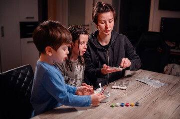 Focused siblings engage in a chemistry experiment with the help of a young woman, depicting a scene of shared learning and family bonding at home