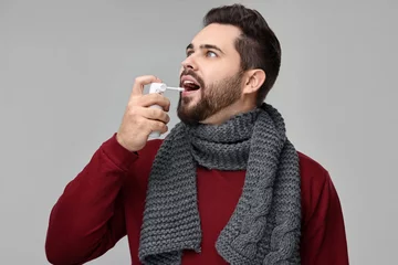 Fotobehang Young man with scarf using throat spray on grey background © New Africa
