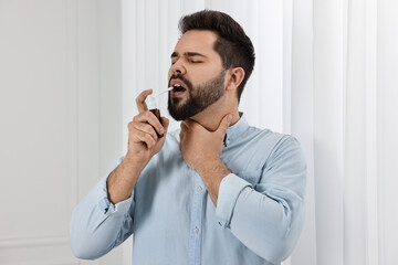 Young man using throat spray at home