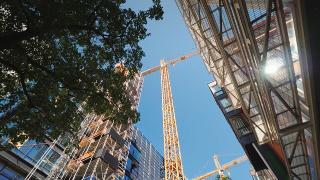 Tower crane in the business district of the modern city. In the windows of office buildings the sun is reflected. Low angle wide shot