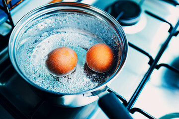 Saucepan stainless steel with two boiling eggs breakfast in a water on a gas stove top view.