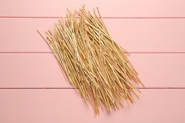 Heap of dried hay on pink wooden background, flat lay