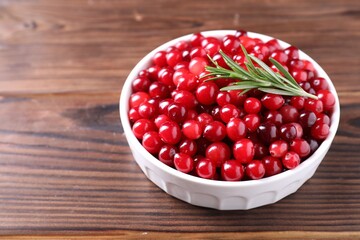 Fresh ripe cranberries and rosemary in bowl on wooden table, closeup