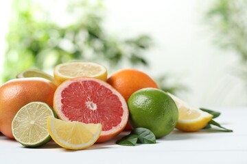 Different fresh citrus fruits and leaves on white table against blurred background, closeup