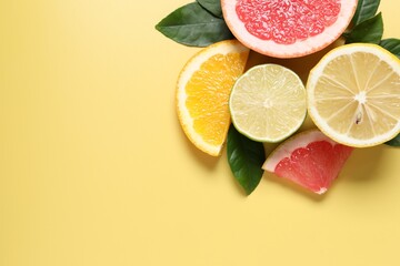 Different cut citrus fruits and leaves on yellow table, flat lay. Space for text