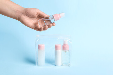 Cosmetic travel kit. Woman putting small bottle with personal care product into plastic bag against light blue background, closeup. Space for text