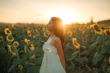 Young carefree asian woman exhaling fresh air in field with sunflowers in sunset, enjoying nature,...