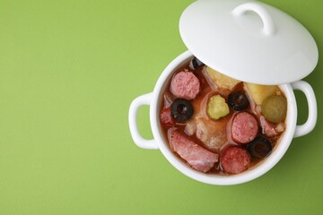 Meat solyanka soup with thin dry smoked sausages in pot on light green background, top view. Space for text