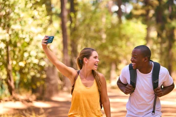 Fototapeten Couple Hiking Along Trail In Countryside Posing For Selfie Or Filming Video On Mobile Phone © Monkey Business