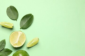 Whole and cut fresh ripe limes with leaves on light green background, flat lay - obrazy, fototapety, plakaty