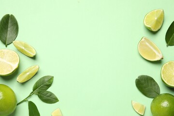 Whole and cut fresh ripe limes with leaves on light green background, flat lay