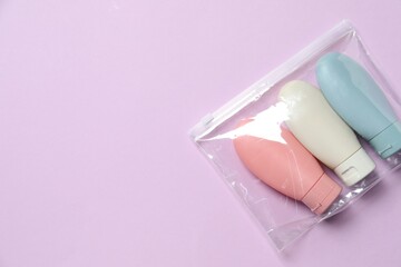 Cosmetic travel kit in plastic bag on violet background, top view. Space for text