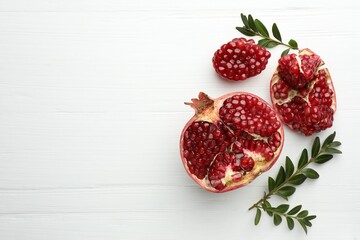 Pieces of fresh pomegranate and branches on white wooden table, flat lay. Space for text