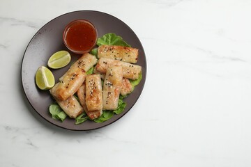 Tasty fried spring rolls and sauce on white marble table, top view. Space for text