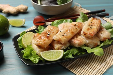 Tasty fried spring rolls, lettuce and lime on light blue wooden table, closeup