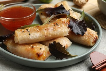 Tasty fried spring rolls, lettuce and sauce on grey table, closeup