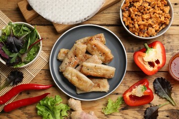 Tasty fried spring rolls and ingredients on wooden table, flat lay