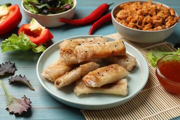 Tasty fried spring rolls and ingredients on light blue wooden table, closeup
