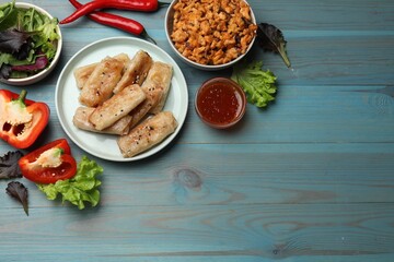 Tasty fried spring rolls and ingredients on light blue wooden table, flat lay. Space for text