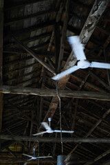 Ceiling Fans in an Old Wooden Attic. Two ceiling fans hang from the wooden beams of an aged attic,...