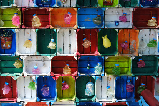 Colorful Wooden Boxes with Recycled Bottles A wall of multicolored wooden boxes, each containing compressed plastic bottles or decorative elements, symbolizing creative recycling.