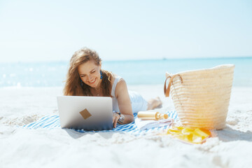 smiling modern woman on ocean coast using laptop