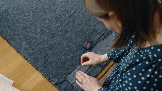 Focused woman pins pattern pieces onto fabric, preparing to tailor a garment on a wooden sewing table.