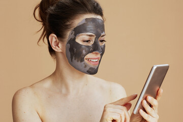 smiling young woman with facial mask using smartphone
