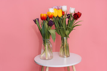 Two bouquets of tulips in a glass vase on a white round table opposite a pink background.