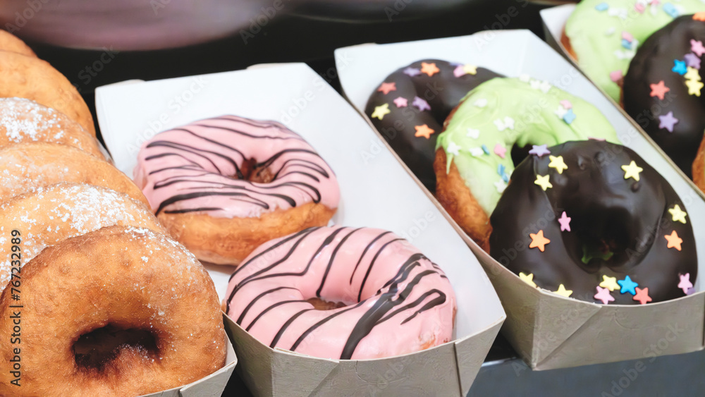 Poster A tray of donuts with pink frosting and chocolate sprinkles. The donuts are arranged in a row and are displayed in a box