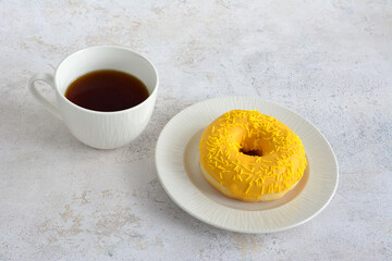 a donut with yellow frosting and a cup of coffee