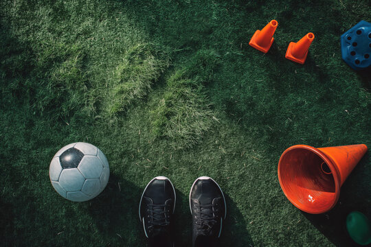 Flat Lay Image of Soccer Training Equipment Lying on Grass Field. Football Cleats, Cones and Ball on the Pitch
