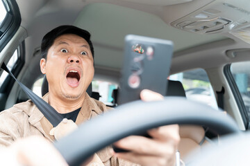 A man is driving a car and looking at his cell phone. He is surprised and excited.