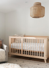 A baby crib in the nursery with neutral tones and a natural wood color with white linens. A wicker pendant light hangs above it from the ceiling,  minimalist decor, a blank white wall with copy space.