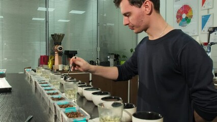 Skilled barista samples coffee using spoon during tasting session. Inspector dips spoon into boiling water before each subsequent cup